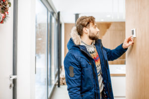 Man wearing winter coat while checking thermostat