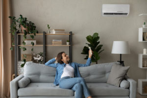 Smiling woman using air conditioner remote climate controller, switching setting comfortable temperature in modern living room