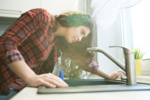 woman looks at possible leak in kitchen sink or faucet