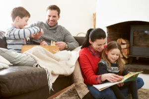 Family Relaxing Indoors Playing Chess And Reading Book Smiling